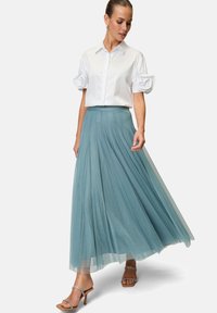 Maxi gonna in tulle azzurro chiaro abbinata a una camicia bianca con maniche a sbuffo. L'outfit è completato da sandali con cinturini.