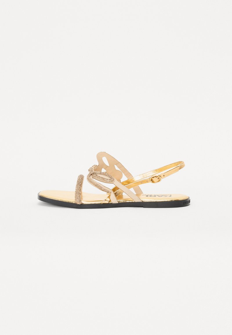 Gold sandals featuring a flat sole, multiple straps, embellished detailing, and a patterned cut-out design on the upper.