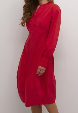 Czerwona sukienka do kolan o luźnym kroju, z długimi bufkami, częściowym plisowaniem na guziki i gładką, błyszczącą fakturą materiału.