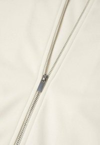 Prenda blanca con cremallera y una textura de tela suave. El hardware de la cremallera plateada se extiende por el centro, creando un aspecto limpio y moderno.