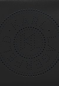 Black leather accessory featuring perforated circular design with decorative text and patterns. Textured surface with smooth finish.