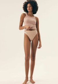 Beżowy prążkowany top na ramiączkach i majtki z wysokim stanem, o dopasowanym kroju. Gładka tekstura z delikatnym połyskiem, noszone na bosaka.