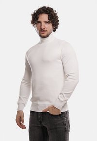 Maglione bianco a collo alto con un modello di maglia testurizzata, polsini e orlo a coste. Indossato con jeans in denim scuro, dal design aderente.
