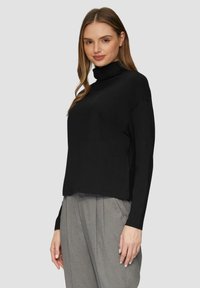 Zwarte coltrui met lange mouwen, gemaakt van zachte stof. Kenmerkt zich door een losse pasvorm en een afgeronde zoom, gestyled met grijze hoge taille broeken.