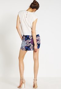 Top bianco a maniche corte con tessuto testurizzato e dettaglio a occhiello sulla schiena. Abbinato a una mini gonna blu a fantasia e tacchi beige.