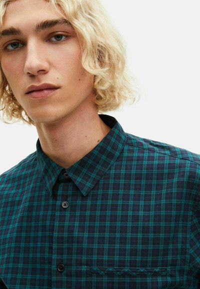 Camicia a quadri blu e verde con colletto classico, dotata di una tasca a sinistra e bottoni neri su un tessuto morbido e textured.