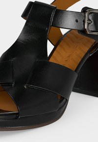 Μαύρο δερμάτινο σανδάλι με φαρδιές μπροστινές λουρίδες, ρυθμιζόμενο λουράκι στον αστράγαλο με ασημένια αγκράφα και χαμηλό πάτο πλατφόρμας.