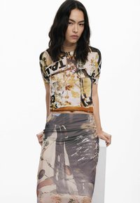 Multifarvet cropped top med blomster- og grafiske tryk; parret med en semi-gennemsigtig, mønstret, rynket lang nederdel. Teksturen virker glat.