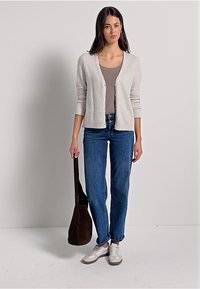 Ljusgrå kofta med ribbad textur, knäppt fram, bärs över en beige topp. Matchad med blå jeans och vita sneakers, håller en brun väska.