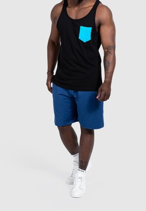 Canotta nera con una tasca blu brillante, abbinata a pantaloni corti blu. Presenta una vestibilità comoda e sneakers bianche con calzini a fantasia.