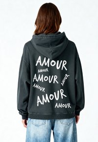 Felpa grigia con cappuccio caratterizzata da testo bianco sparso che recita "AMOUR" in diverse dimensioni e orientamenti sul retro. Ampia tasca frontale, polsini a coste.