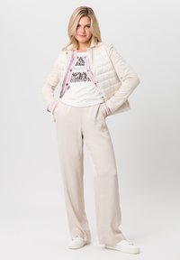 Lichte, crèmekleurige pufferjack met contrasterende roze accenten, gecombineerd met beige, luchtige broeken en witte sneakers.