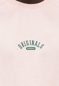 Ροζ ανοιχτό φούτερ με ριμπ κολάρο, με πράσινη κεντημένη επιγραφή που γράφει «ORIGINALS ADIDAS» σε τόξο.