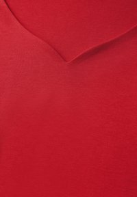 Červená bavlněná tkanina s hladkým povrchem, s mělkým designem ve tvaru V. Materiál vypadá jemně a má jednotnou barvu.