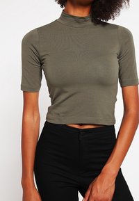 Haut court vert olive à col montant et manches courtes, en tissu extensible doux, coupe ajustée et texture lisse.