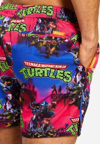 Dvojfarebné plavky s výrazným dizajnom Teenage Mutant Ninja Turtles na ružovom pozadí. Elastický pás s bočnými vreckami.
