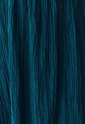 Teksturovana tkanina v globoki smaragdni barvi z navpičnimi gubami, ki prikazuje naguban videz in neenakomerno površino. Rahlo odraža ambientno svetlobo.