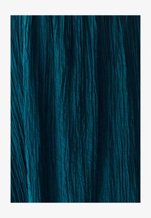 Teksturovana tkanina v globoki smaragdni barvi z navpičnimi gubami, ki prikazuje naguban videz in neenakomerno površino. Rahlo odraža ambientno svetlobo.