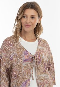 Cardigan cu model paisley brown și mov, cu un sistem de legare în față, fabricat dintr-un material ușor și cu o textură moale, purtat deasupra unei bluze albe.