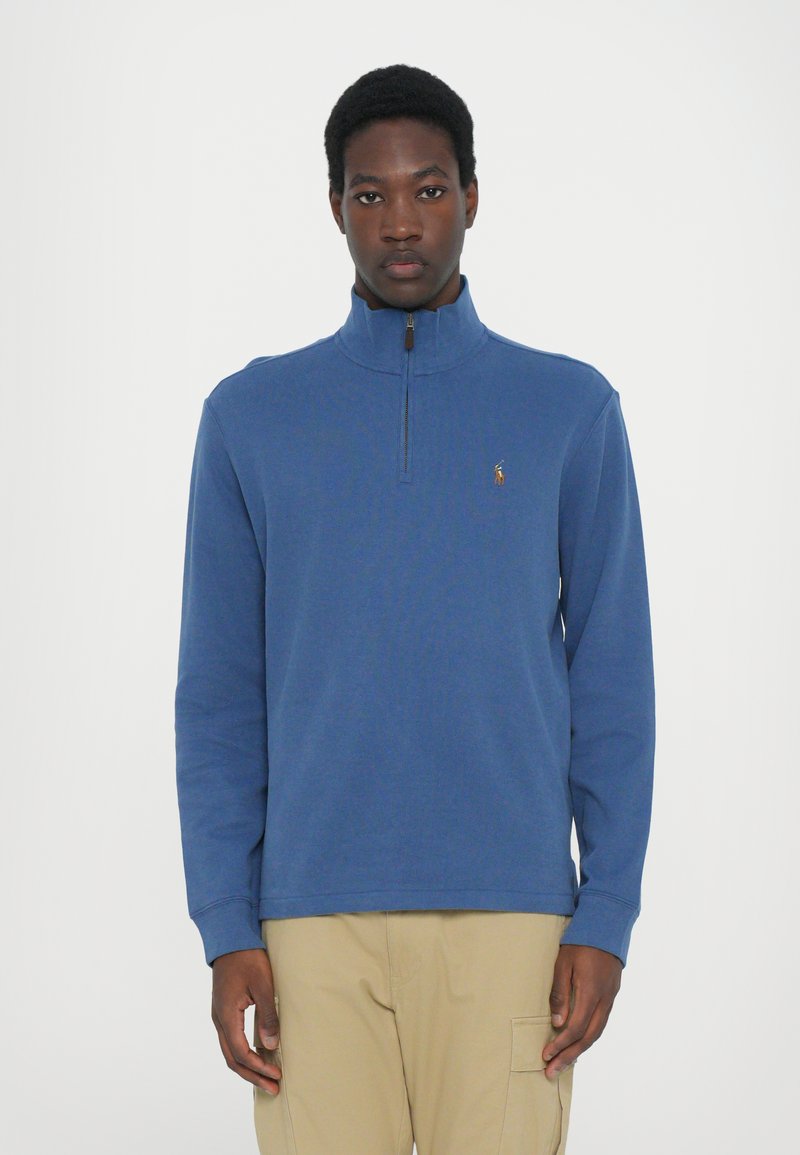 Blauwe fleece pullover met een hoge kraag en een halve rits, met een klein logo op de borst. Zachte textuur en een ontspannen pasvorm.