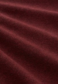 Bordeauxrot strukturiertes Strickgewebe mit einem dezenten Muster, das eine weiche und glatte Oberfläche zeigt, die sanfte Falten und Drapierungen aufweist.