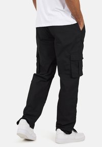 Czarne spodnie cargo wykonane z trwałego materiału, z bocznymi kieszeniami, prostym krojem nogawek, noszone z białymi trampkami.