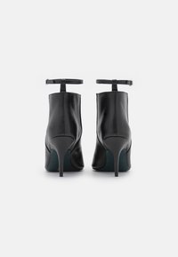 Botines de cuero negro hasta el tobillo con punta afilada, tacón de aguja y correa ajustable en el tobillo. Textura suave y diseño estilizado.