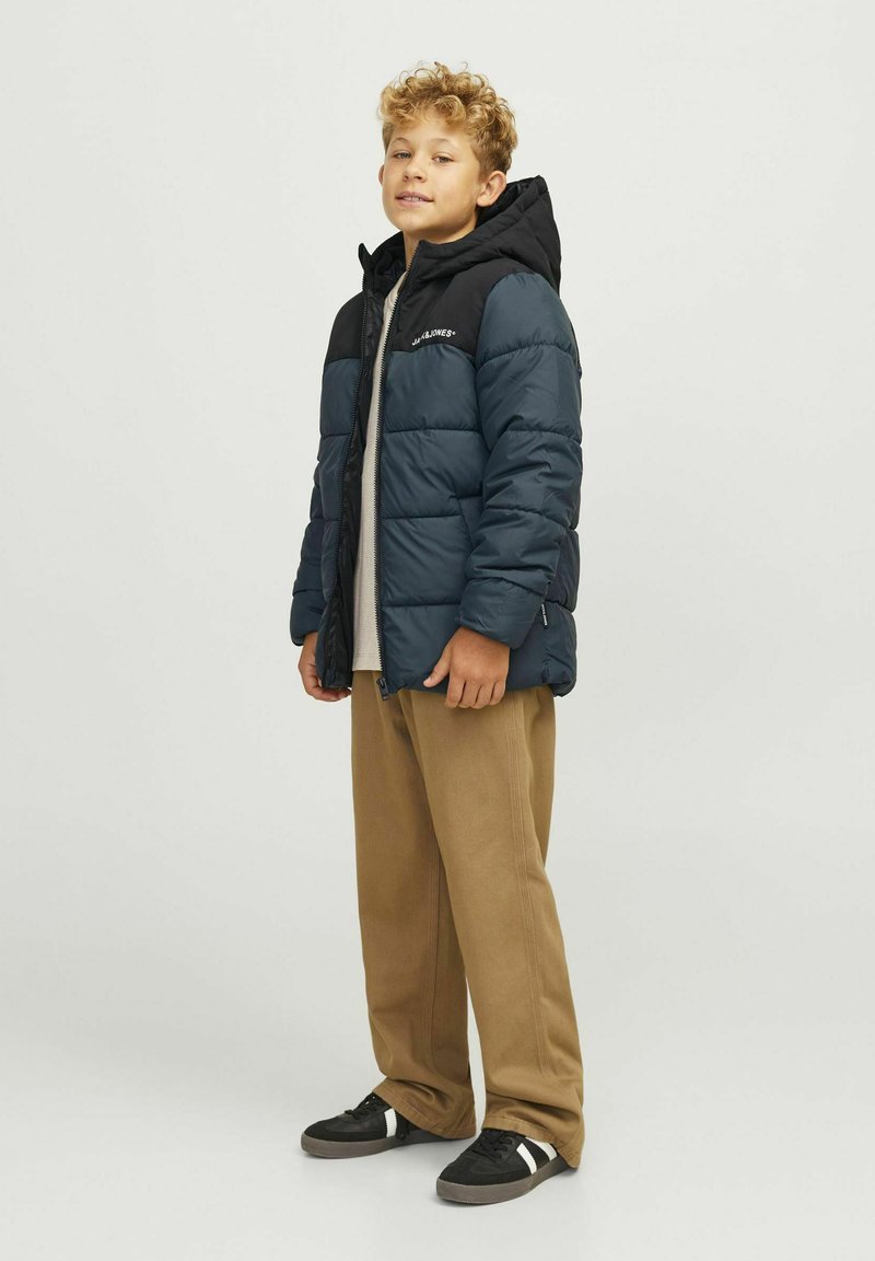 Pufjakas ar tumši zilu un melnu paneļu, ar kapuci un rāvējslēdzēju. Apvienots ar beidzīgas krāsas biksēm un melniem sneakers.