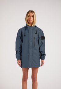 Chaqueta resistente al agua en azul oscuro, con un alto cuello, capucha ajustable con cordón, puños elásticos y un bolsillo en el pecho con cremallera.