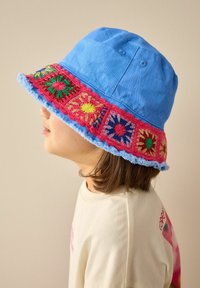 Blauer Bucket Hat mit einem bunten gehäkelten Band, das florale Muster aufweist. Unvollendeter Rand in Hellblau. Weicher Stoff.