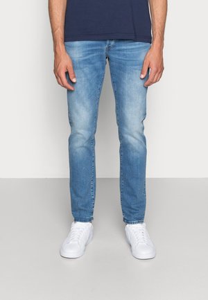 Hellblaue Jeans im Slim Fit mit leichten Used-Effekten und kontrastierendem Nähten, kombiniert mit weißen Sneakern.