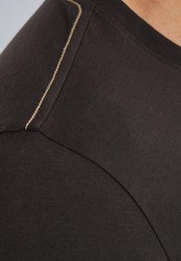 Camiseta negra con una textura suave y costuras doradas contrastantes a lo largo de la costura del hombro, con un diseño de cuello redondo clásico.