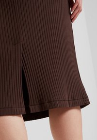 Brauner, gerippter Strickrock mit Seitenschlitz. Verfügt über eine strukturierte Oberfläche und einen geraden Saum. Der Stoff ist dehnbar und figurbetont.