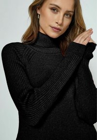 Schwarzer gerippter Rollkragenpullover mit langen Ärmeln, der einen hohen Kragen und strukturierte Stoffe aufweist und ein figurbetontes Design und eine elegante Silhouette präsentiert.