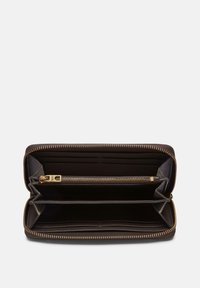 Portafoglio in pelle marrone con zip dorata, scomparto con cerniera e più slot per carte. L'interno presenta una texture liscia e ampio spazio.