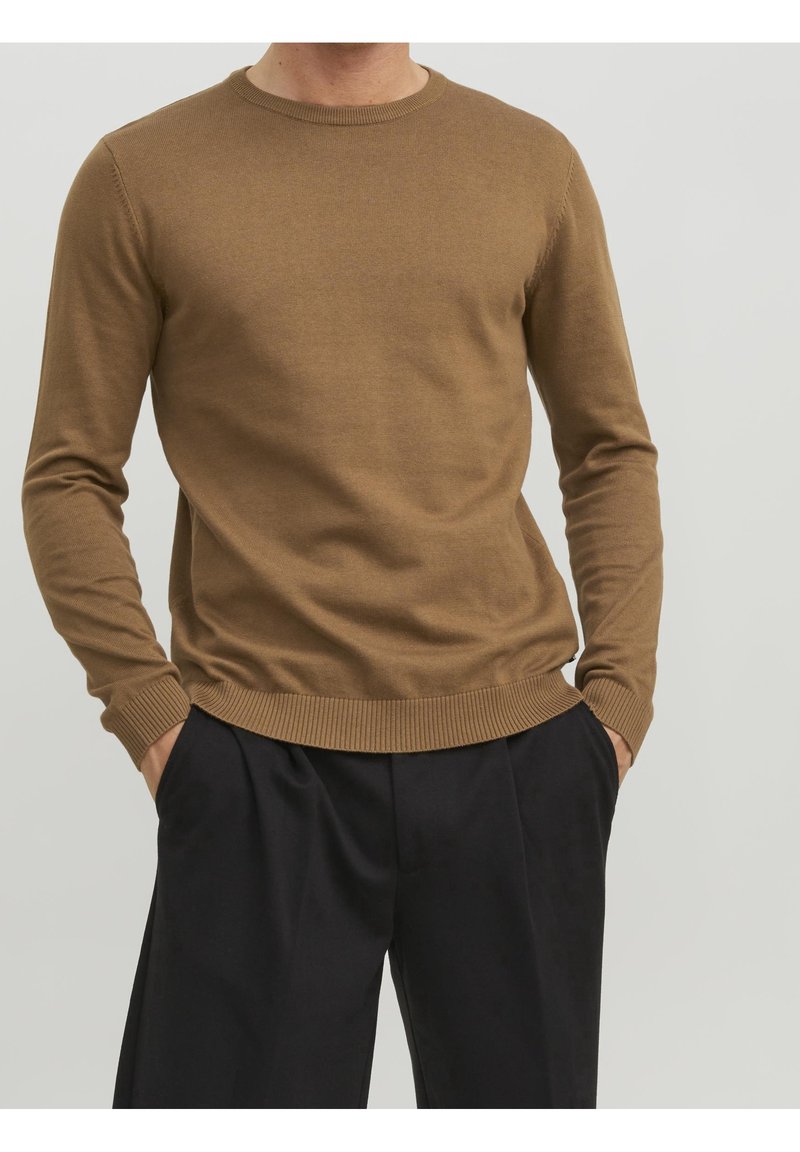 Brown crewneck sweater made of soft material, featuring ribbed cuffs and hem. Worn over dark pants, showcasing a fitted silhouette.