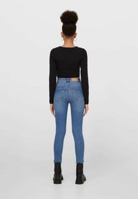 Top negro de manga larga combinado con vaqueros pitillo azul de talle alto y botas negras; presenta un diseño ajustado, forma ceñida de leggings y bolsillos traseros.