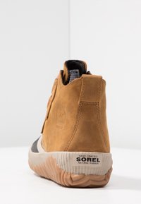 Bottine en cuir marron avec une semelle en caoutchouc texturée et un patch logo. Présente un dos haut incurvé et une doublure en tissu noir.