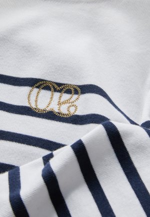 White fabric with navy horizontal stripes, featuring a gold embroidered "O" accent. The texture appears smooth and soft.