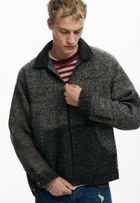 Texturierte gewobene Jacke mit einem dunklen Grundton und mehrfarbigen Akzenten, ausgestattet mit einem Kragen, einem Reißverschluss und einer Fronttasche.