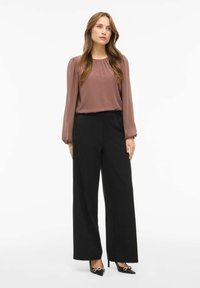 Blusa mauve a maniche lunghe con scollatura arricciata abbinata a pantaloni neri a gamba larga con vita alta. Tacchi a punta neri con dettagli dorati.