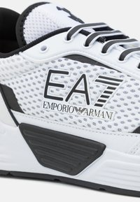 Hvit mesh sneakers med svarte detaljer, en teksturert gummisåle, logodetaljer og slitesterke snøringøyer. Moderne atletisk design.