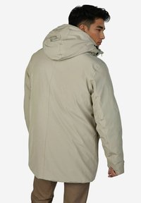 Beige geïsoleerd jack met capuchon, heeft een gladde textuur, recht gesneden en zichtbare stiksels aan de achterkant. Ontworpen voor warmte.