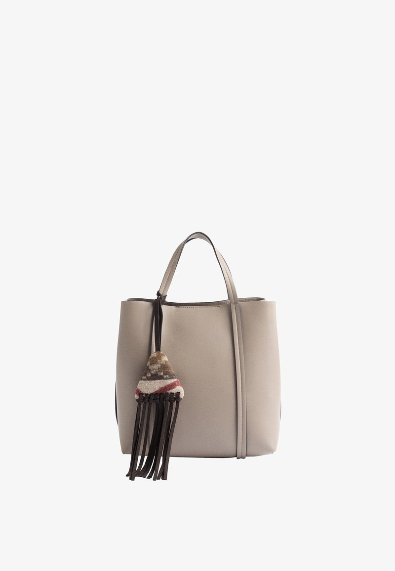 Sac cabas beige avec deux poignées et un pompon en tissu multicolore orné de franges marron suspendu à l'avant.