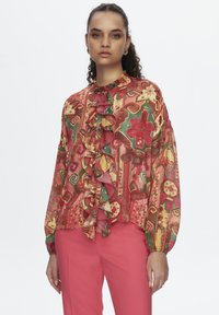Bunt gemusterte Bluse mit floralem Design, Rüsche vorne und langen Ärmeln. Aus einem leichten Stoff gefertigt, mit hohem Ausschnitt.