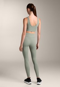 Csíkozott, világoszöld sportmellény és leggings szett, amely illeszkedő fazonú, magas derékkal rendelkezik, fekete sportcipőkkel párosítva.