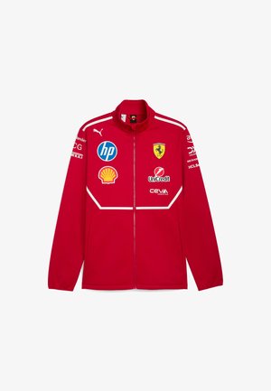 Czerwona kurtka zapinana na zamek z wysokim kołnierzem; posiada loga Ferrari, HP, Shell i innych. Gładki materiał z białymi akcentami i szwami.