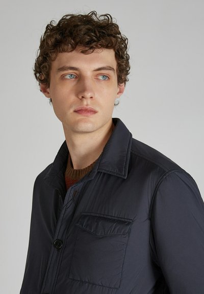 Granatowa, lekka kurtka z zapięciem na guziki, rozpostartym kołnierzem i kieszenią z przodu. Gładka tekstura, minimalistyczny wygląd i dopasowany krój.