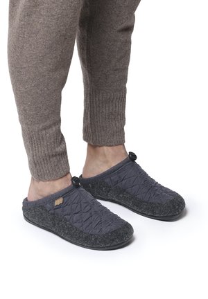 Chaussons en tissu matelassé gris avec une semelle texturée noire, présentant un petit accent supérieur et un détail en tissu gris contrasté.