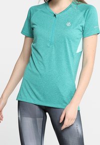 Tyrkysové atletické tričko s krátkým rukávem a zipem na krku; vyrobeno z prodyšného materiálu. Obsahuje logo na levé hrudi a akcenty na bočních panelech.